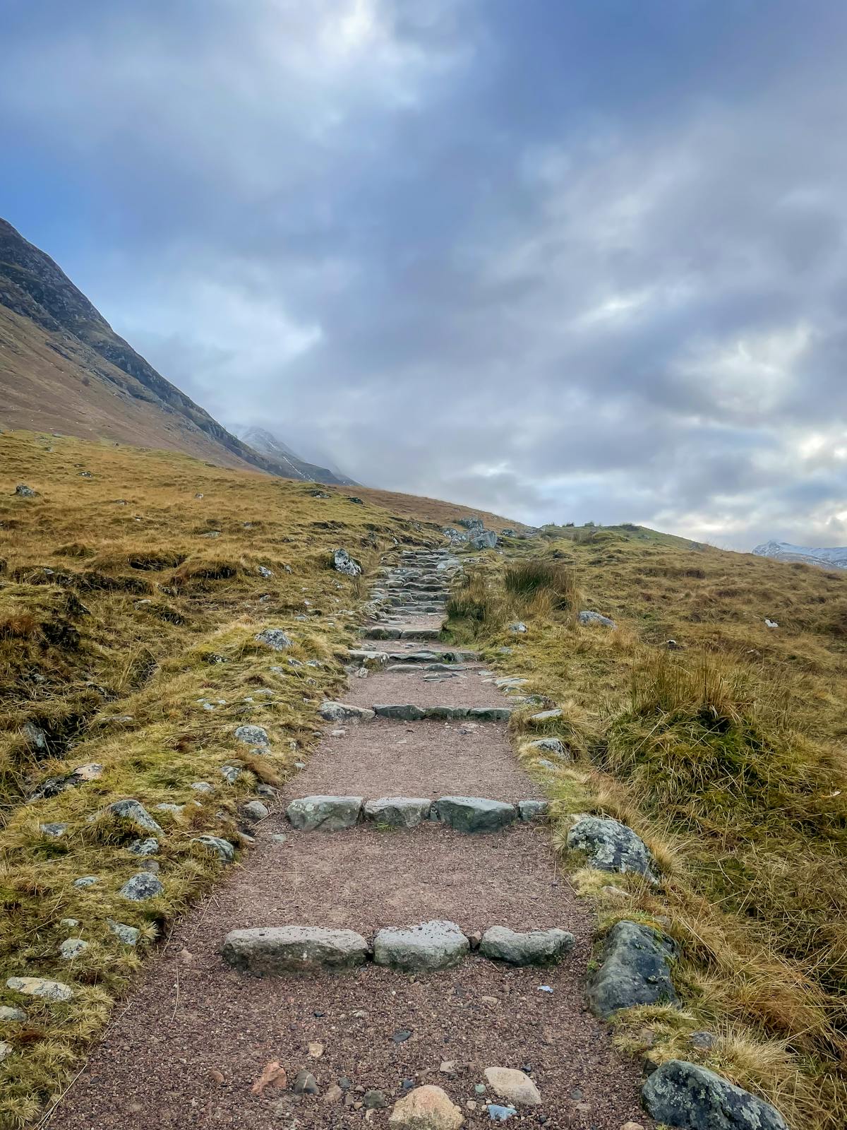 A hiker on a mountain trail in the Scottish Highlands with dramatic peaks in background